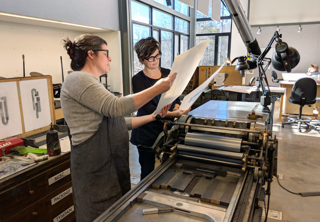 two women examining prints that have just come off a Vandercook press