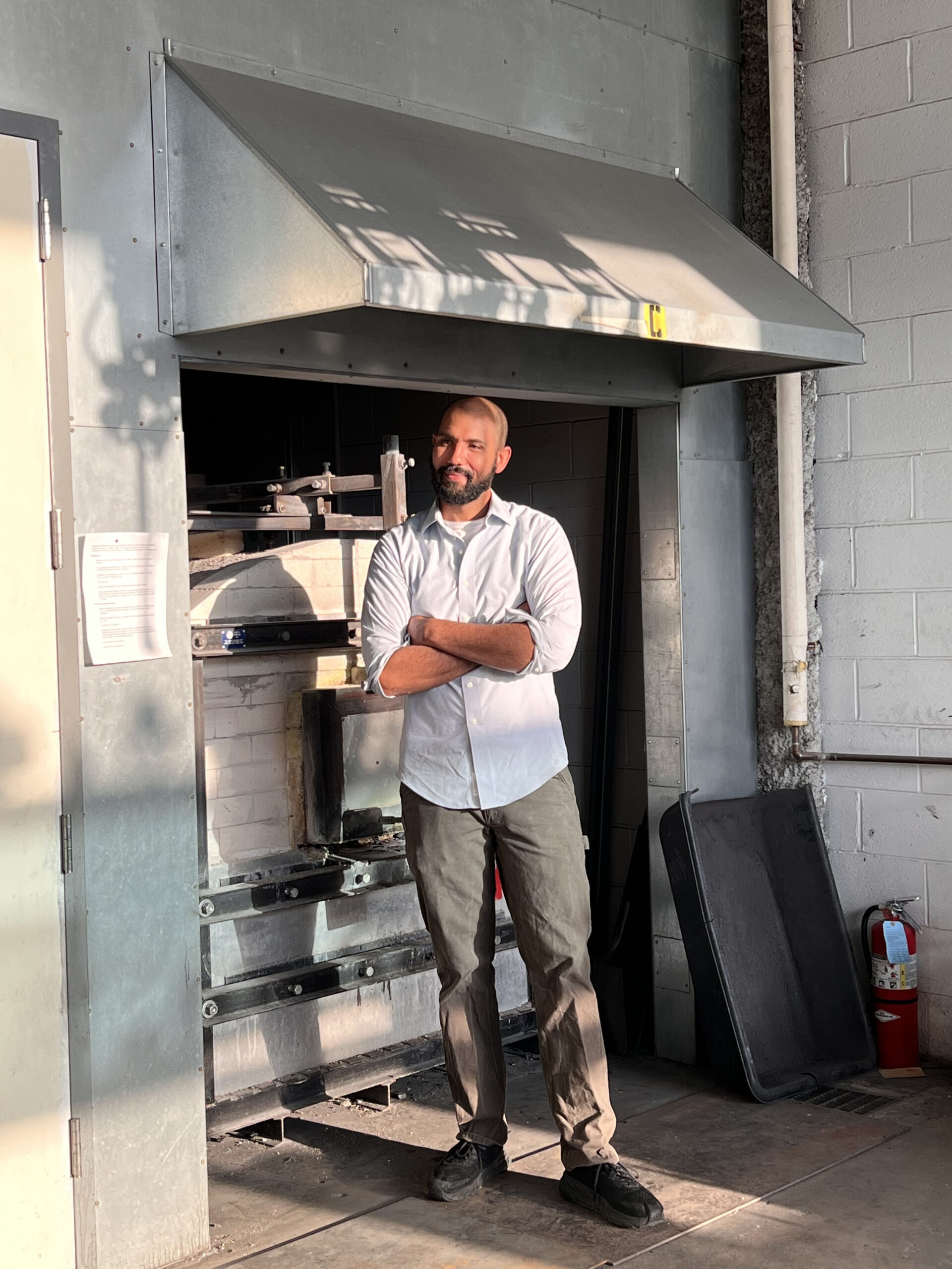 Photo of Jason McDonald in a glass studio. Jason is a young, black man with crossed arms and a warm, pensive expression.